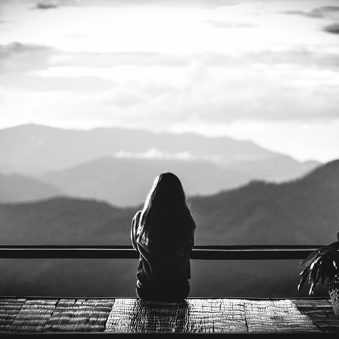 Black and white photo of a woman sitting and looking at mountain scenery - Mastering Alchemy