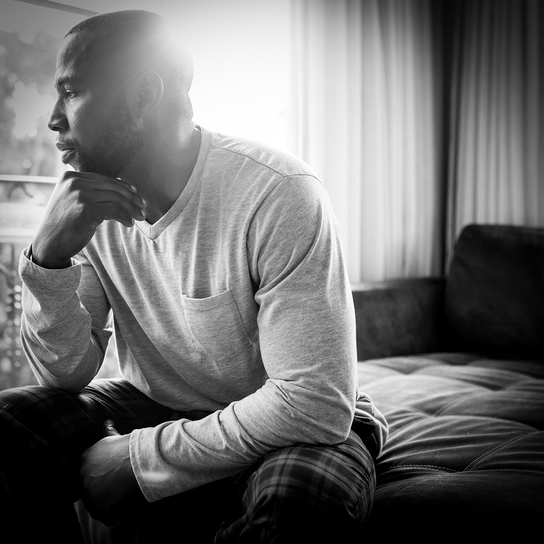 Black and white image of a black man sitting at the corner of the couch